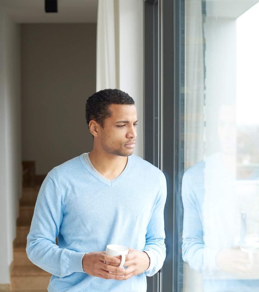 Shot of a handsome man looking pensively out the window while drinking coffee in her modern home